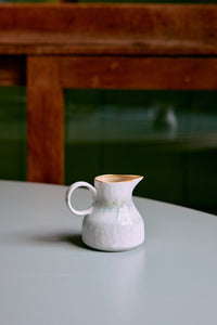 The HKLIVING Petal milk jug displayed on a pale grey table, with a wooden table and green tiled wall in the background