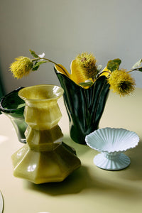 Olive green Silhouette glass vase grouped with other glass and ceramic vases and a scalloped dish as part of a styled tablescape