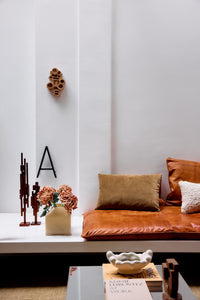 The HKLIVING brutalist wall sculpture displayed above a tan leather sofa, alongside a metal letter 'A', dried flowers in a stoneware vase and wooden sculptural objects