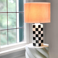 black and white checkered table lamp with pink shade by &k Amsterdam on a sculptural side table
