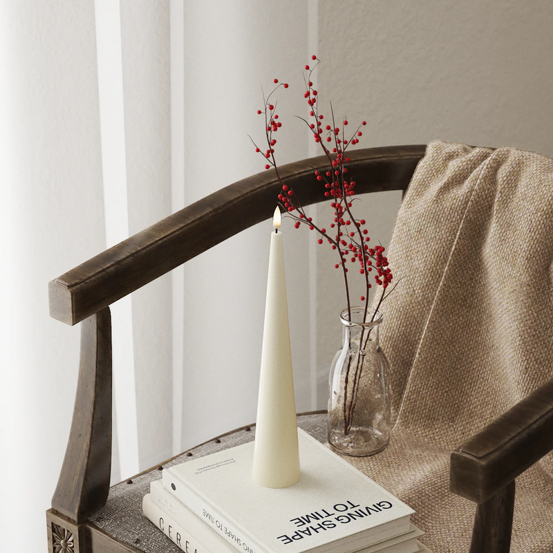 Decorative setup with a candle, vase with red berries, and books on a wooden chair.