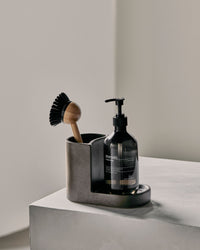 Regular Meraki Datura holder in dark grey with a dish brush and soap pump on a stone plinth