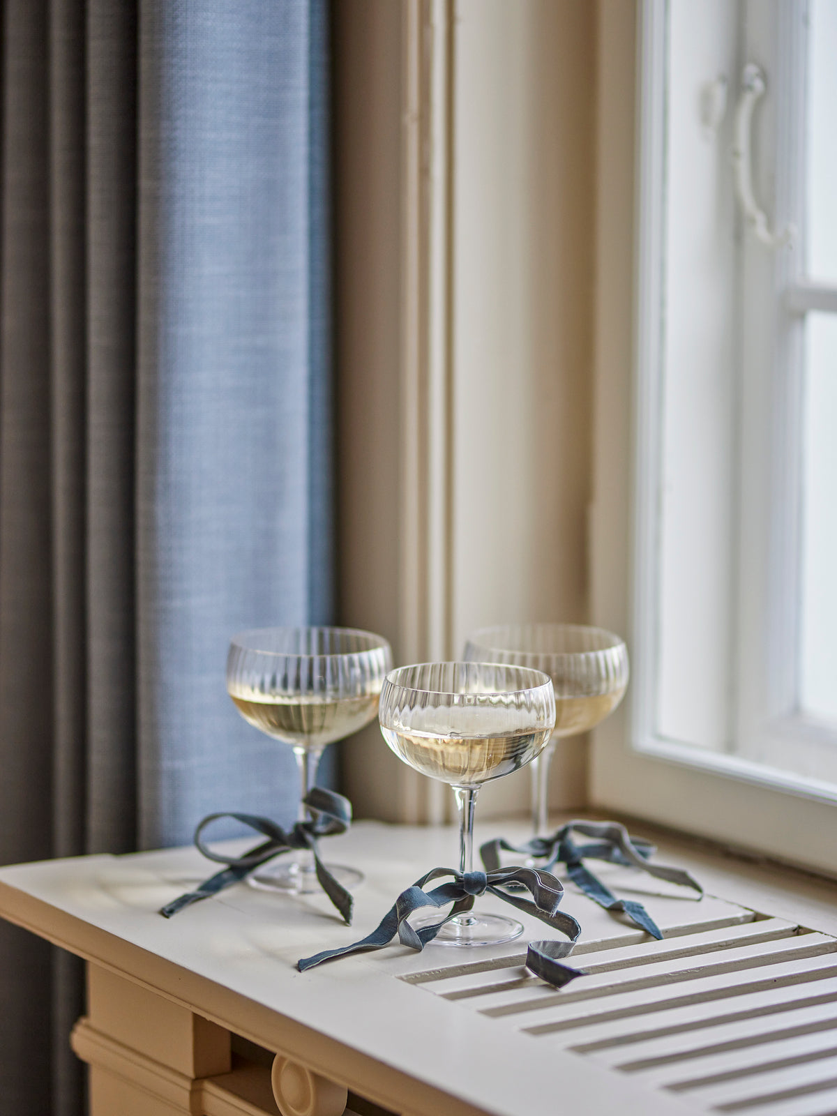 Three glasses of champagne with decorative ribbons on a wooden table near a window.