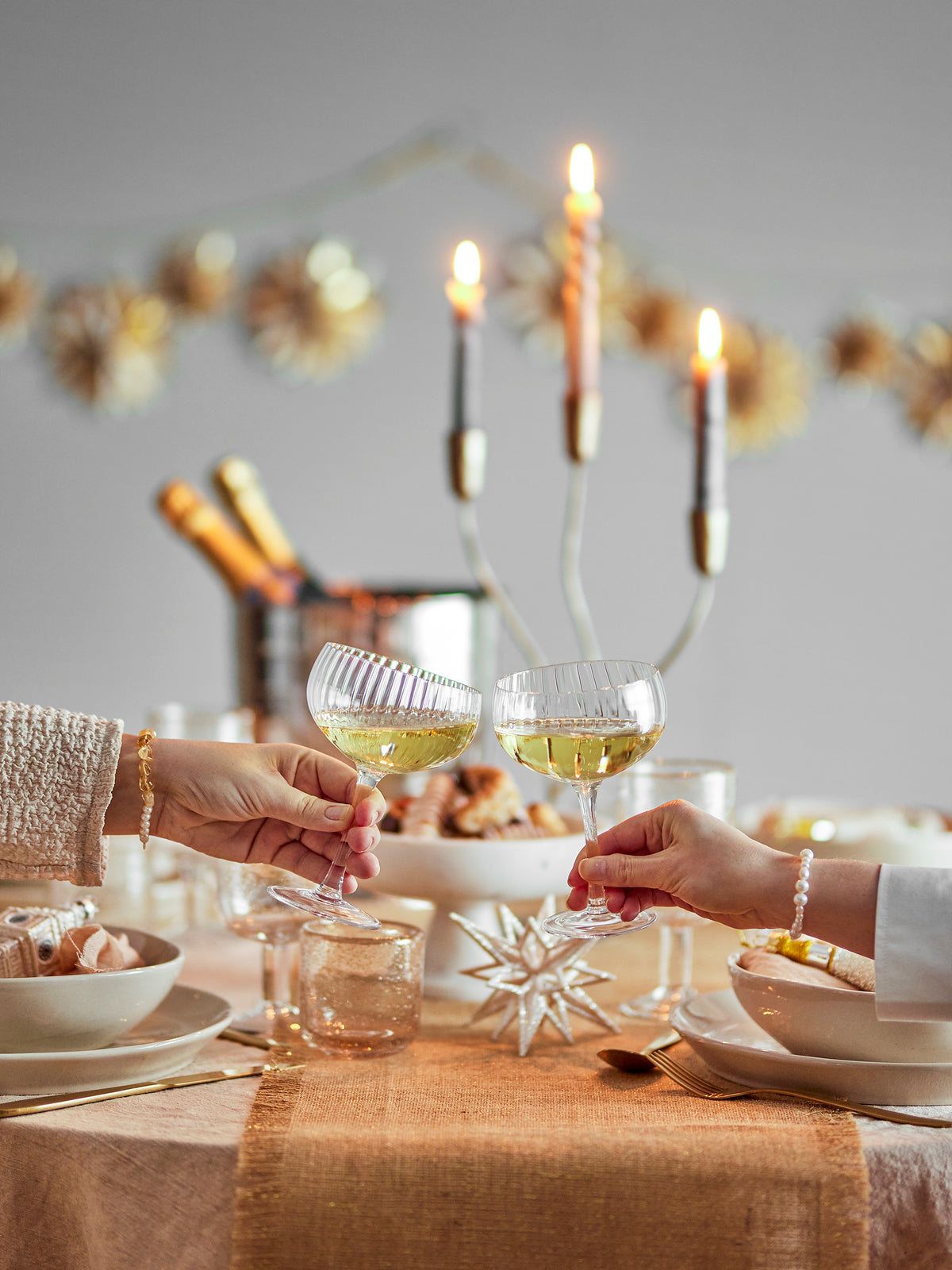 Astrid champagne coupe glasses raised in a toast at a festive candlelit table
