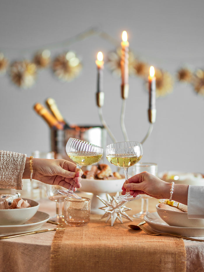 Astrid champagne coupe glasses raised in a toast at a festive candlelit table
