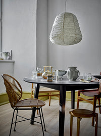 Round dining table set with glassware and stoneware beside a rattan chair, under a white paper pendant light