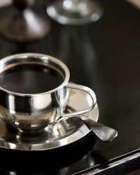 VIREA chrome cup and saucer by Nordal on a dark console table, styled with a candlestick and glass vase