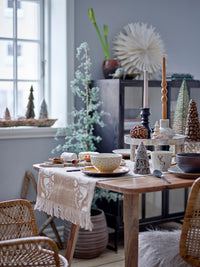 Vita tree standing by a window beside a Christmas dining table set with candles, pine cone decorations and rattan chairs