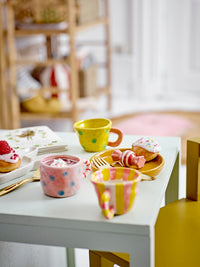 Colorful ceramic cups and saucers on a white table with pastries in a cozy room.