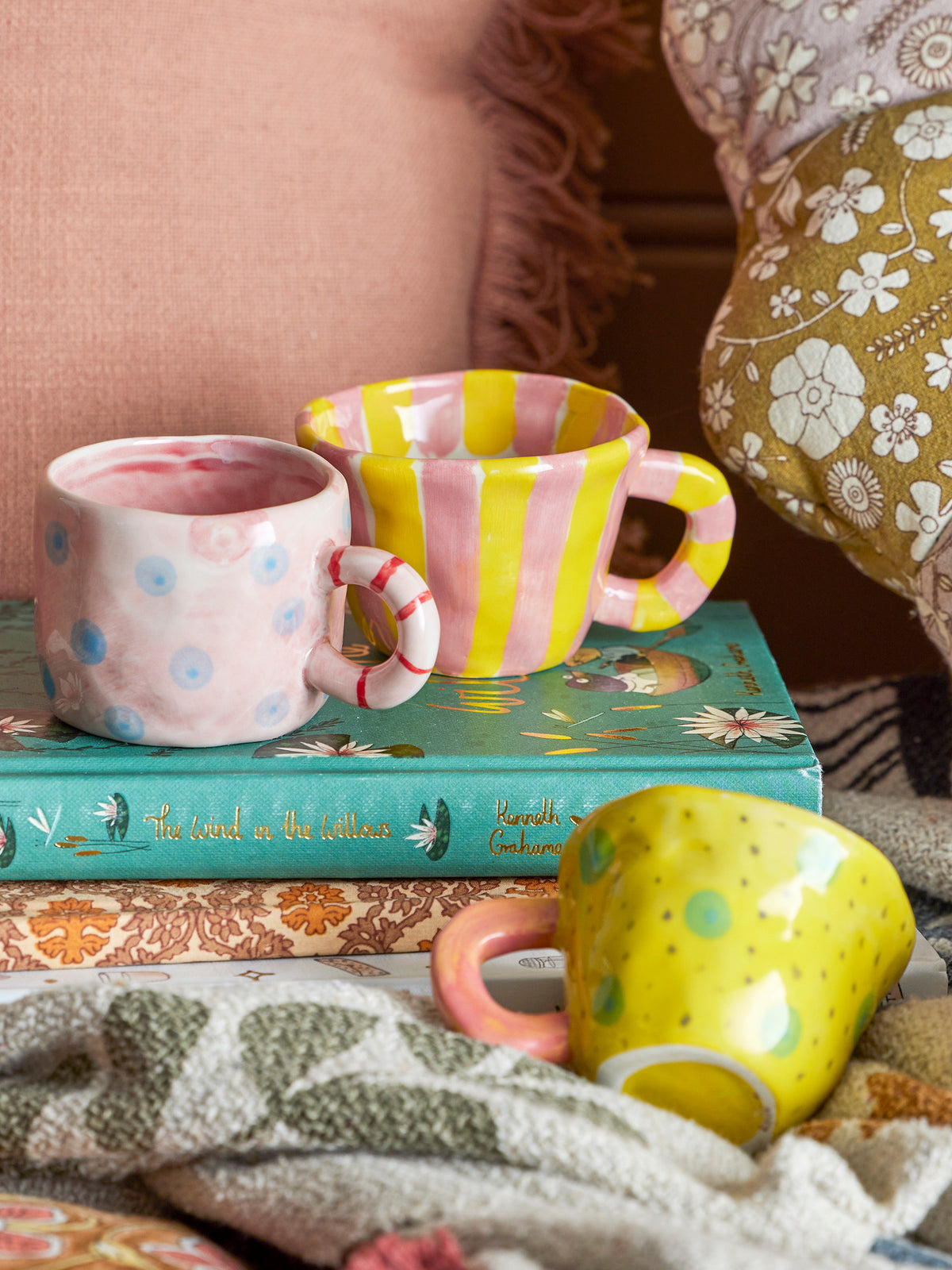 Three colorful mugs on a stack of books with a soft, patterned background