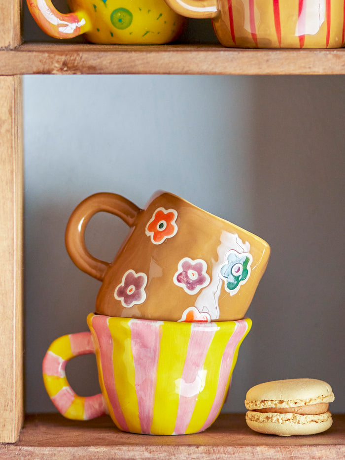 Nini cup pink and yellow stripes, stacked with playful mugs on a shelf
