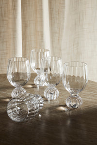 Four Taurin wine glasses on a dark wooden table in front of a linen curtain, with one glass lying on its side