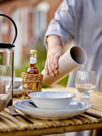 Person pouring a drink into a glass on a table with a bottle and bowl.