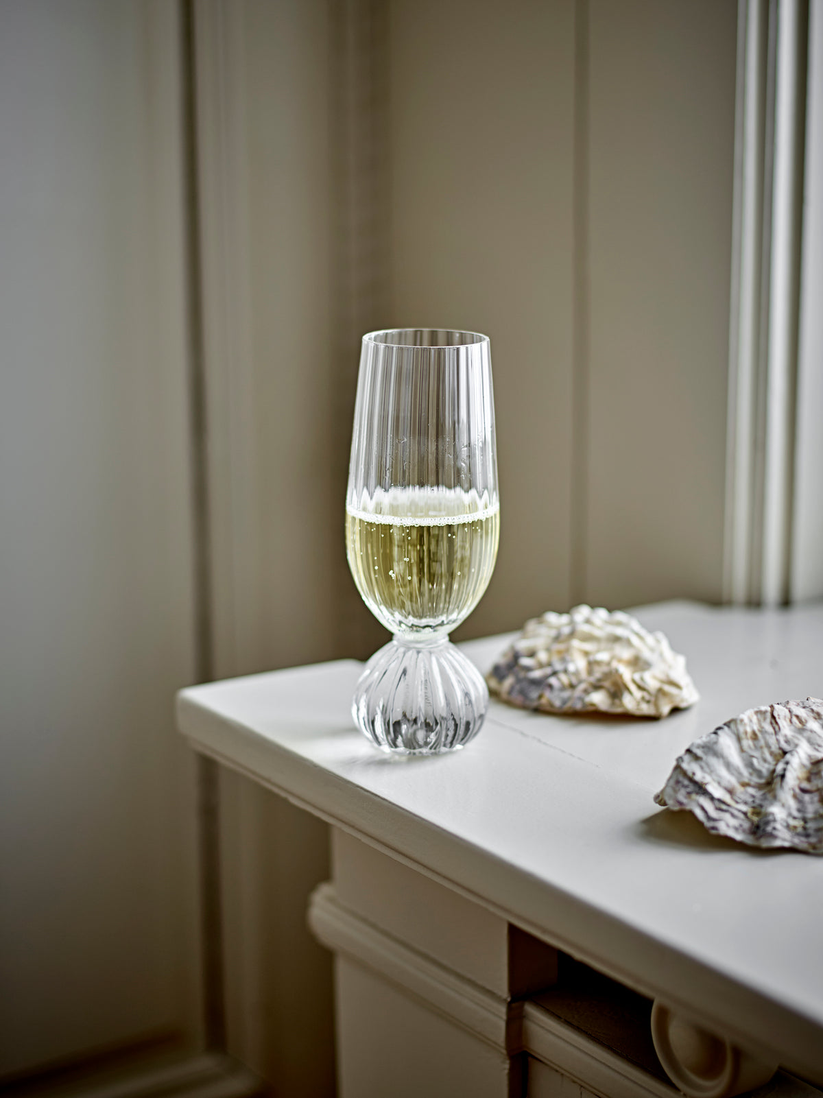 Taurin champagne glass filled with sparkling wine on a white windowsill beside a shell
