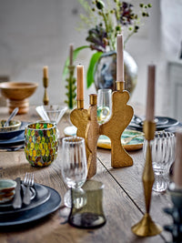 Taurin glassware on a rustic wooden table set with dark plates, brass candlesticks with tapers and a vase of dried stems