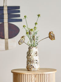 Noble beige vase with pierced texture holding dried wildflowers on a side table