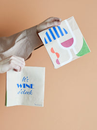 Wine napkins double-sided, one with blue wine quote and one with abstract glass, held in hand
