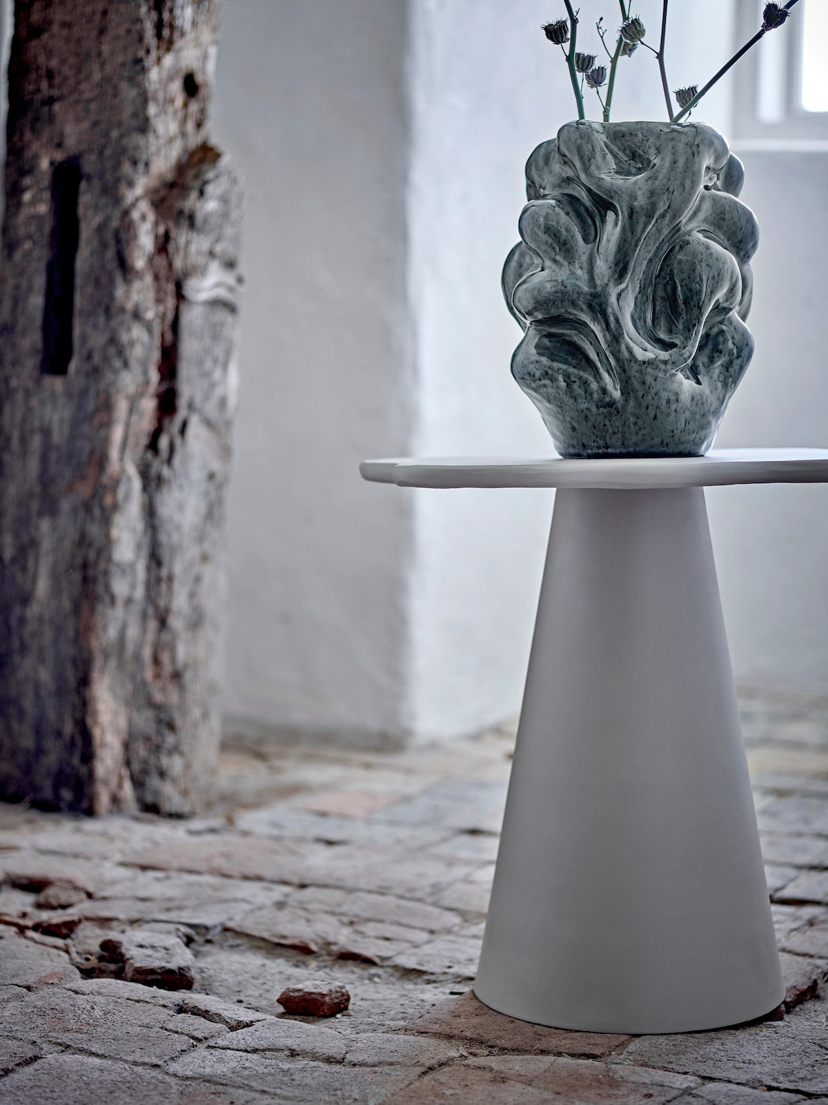 Vuelle grey vase with dried thistle stems on a white pedestal side table