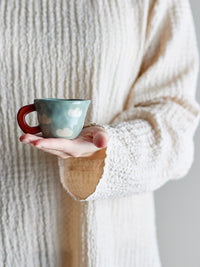 hand holding small blue nini cup with clouds and terracotta handle
