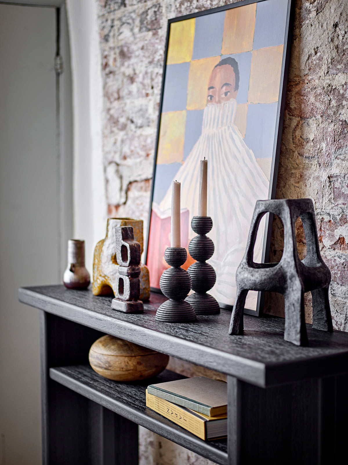 Decorative shelf with sculptures and a framed portrait against a brick wall.