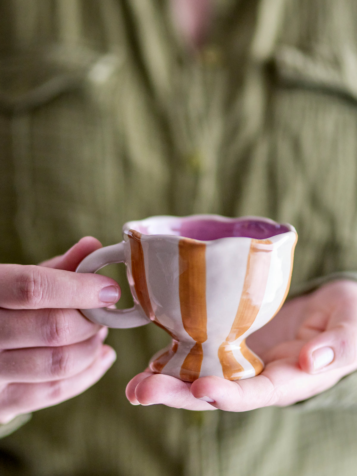 Willa cup in brown and orange striped stoneware with wavy edge, held in hand
