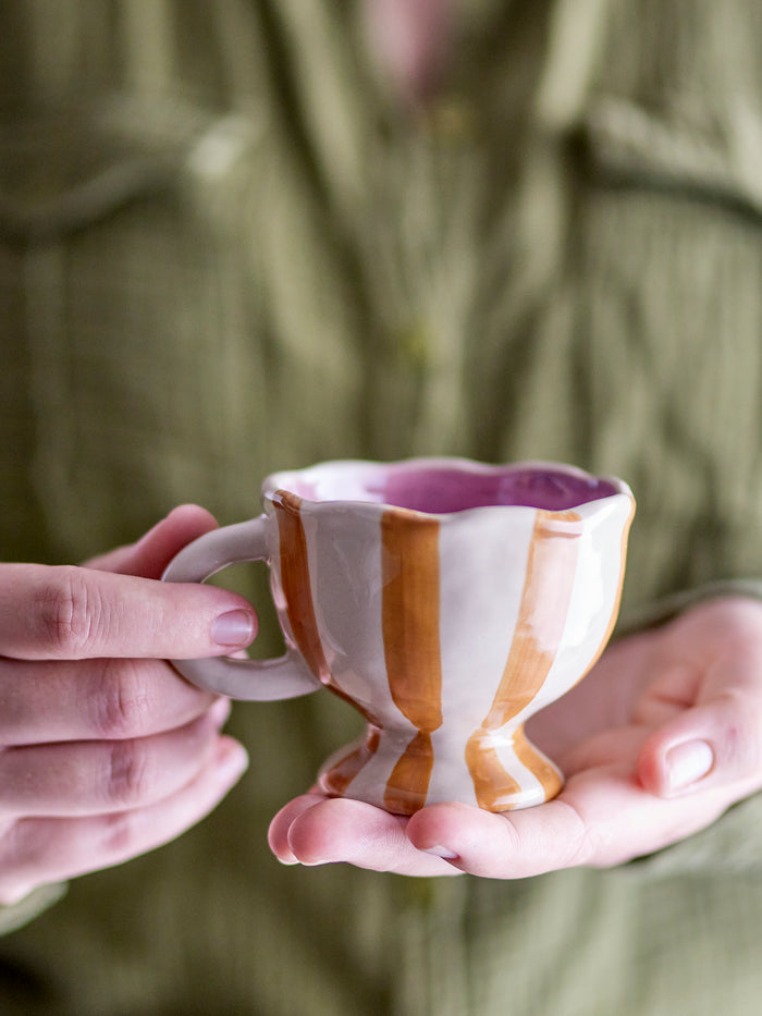 Willa cup in brown and orange striped stoneware with wavy edge, held in hand
