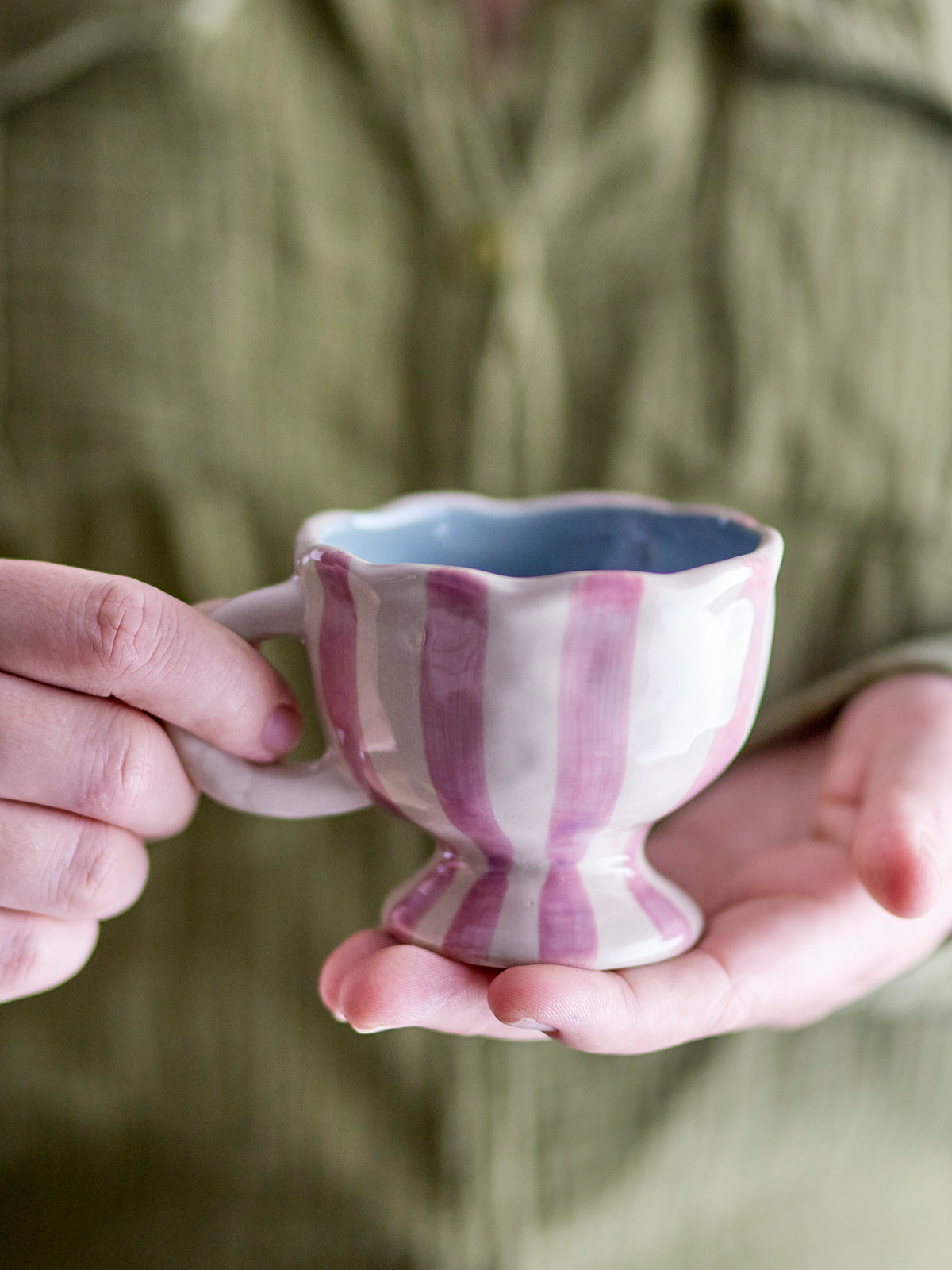 Willa cup in white and pink striped stoneware with wavy edge, held in hand
