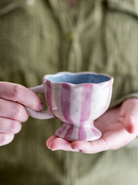 Willa cup in white and pink striped stoneware with wavy edge, held in hand
