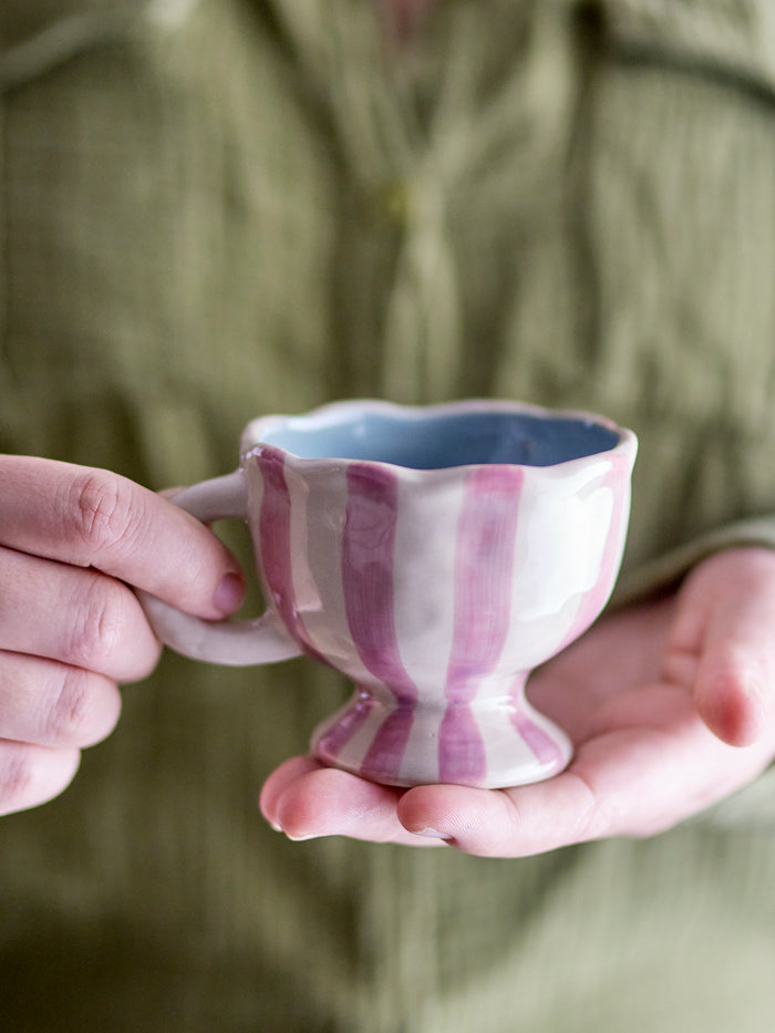 Willa cup in white and pink striped stoneware with wavy edge, held in hand
