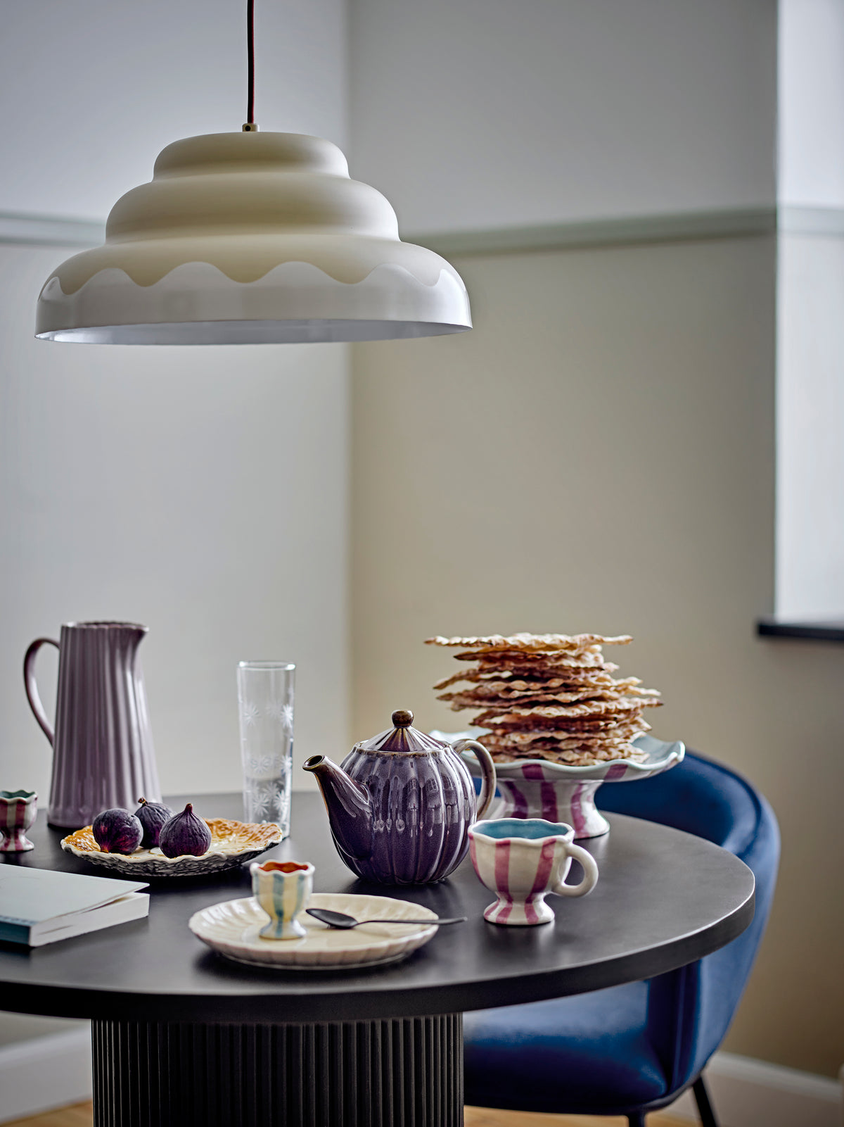 Round dining table with purple teapot, glass, and other items in a room with a pendant light.