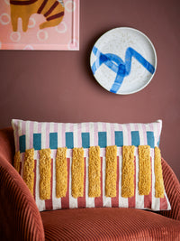 Lane Cushion with piano key like style placed on a rust-coloured armchair against a warm-toned wall
