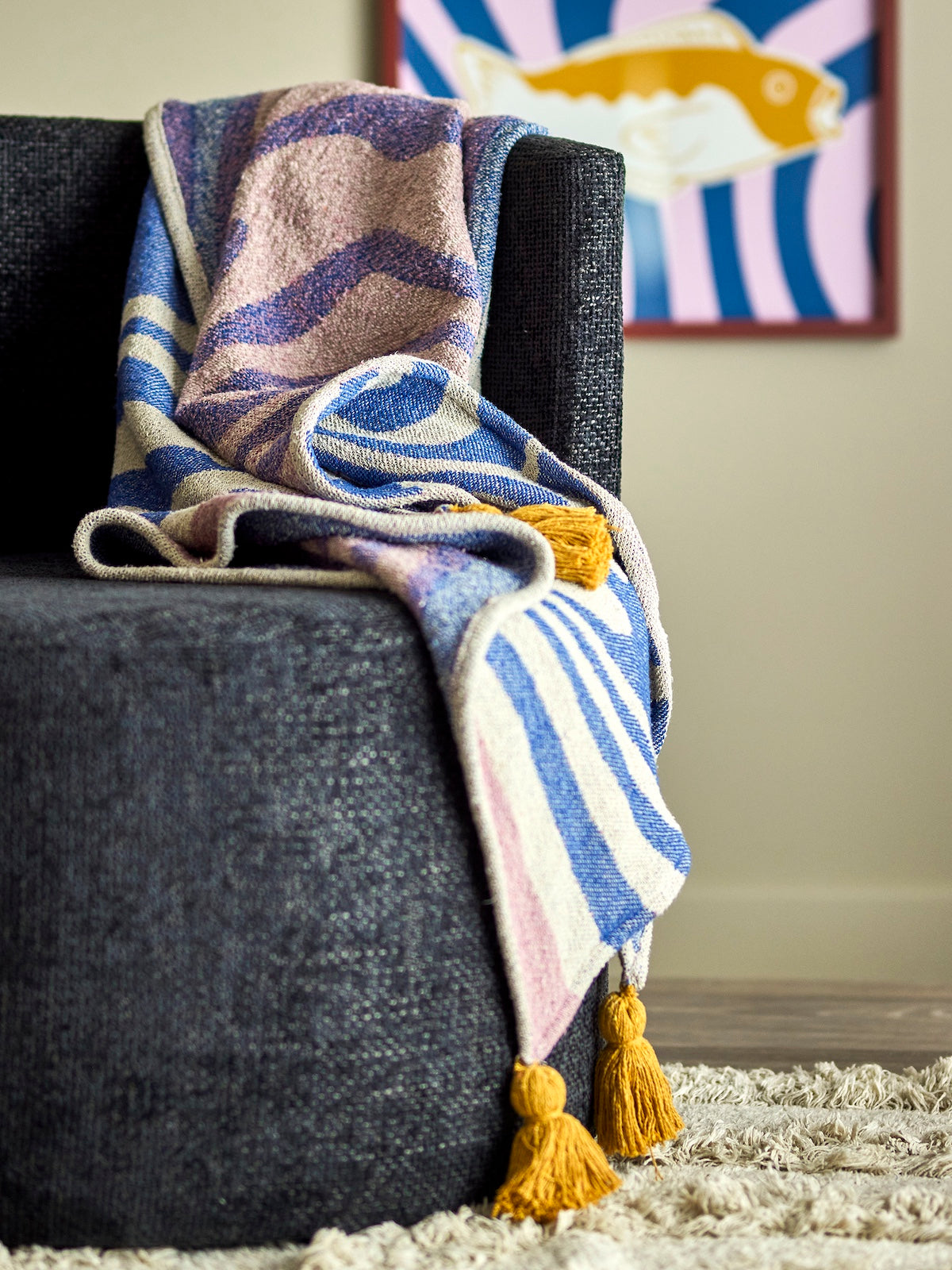 Arlie blue woven throw draped over a dark armchair with tasselled corners