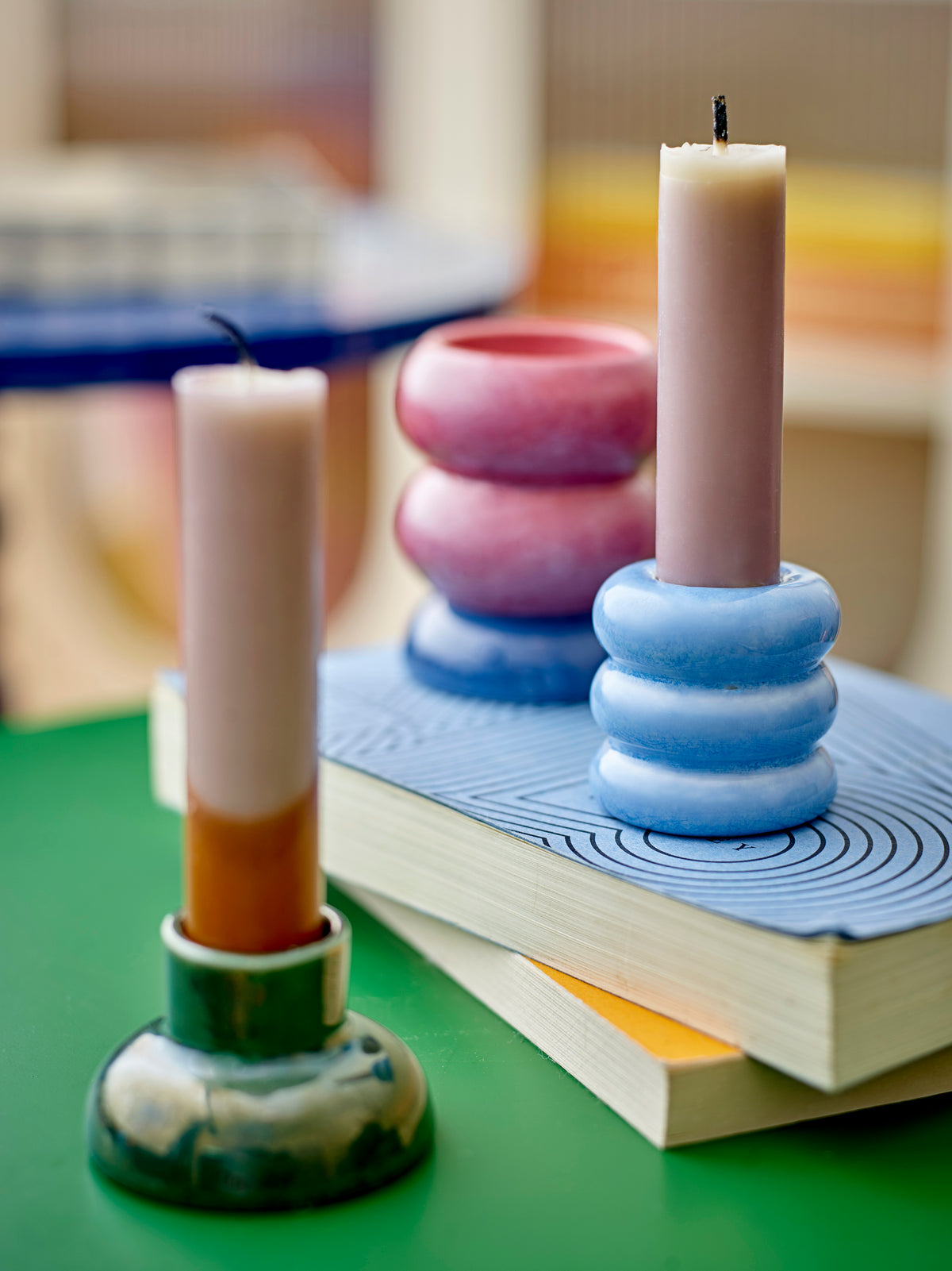 Tana light blue stacked candle holder with a taper candle beside the dusty pink stack on a green table over a pile of books