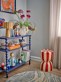 Colourful styled room with blue bobbin-leg shelves, ceramics, a vase of flowers and a red and white striped stool