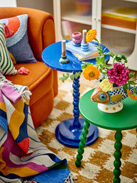 Tana candle holders on a small blue side table beside books and a bright bouquet, next to an orange armchair