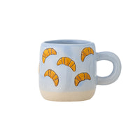 Millie light blue stoneware cup with orange croissant illustrations and a beige base on a white background