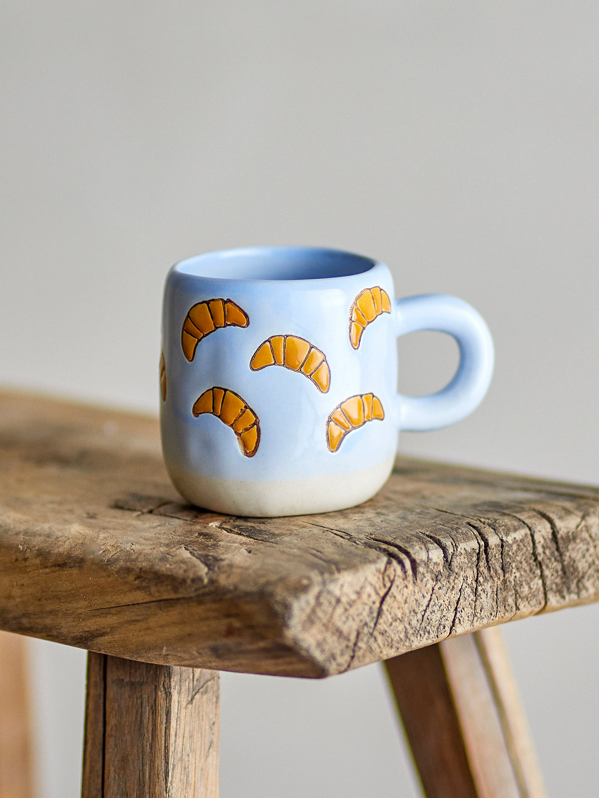 Millie croissant cup on the edge of a rustic wooden stool against a soft grey wall