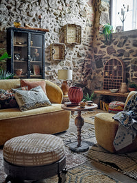 Hazem cabinet styled in a rustic stone-walled living room alongside a mustard sofa, wooden side table and woven wall baskets