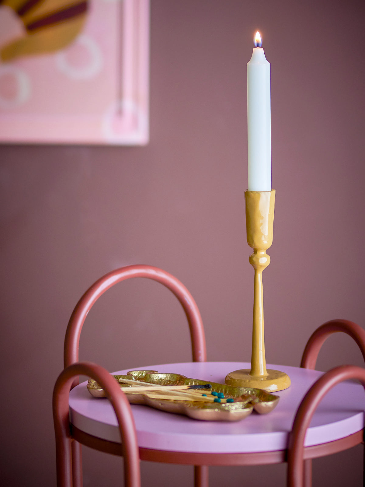 yellow taper candle holder by bloomimgville styled with lit candle on pink table
