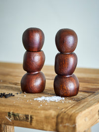Salvi dark wooden salt and pepper mills on a rustic wooden table beside scattered peppercorns and sea salt