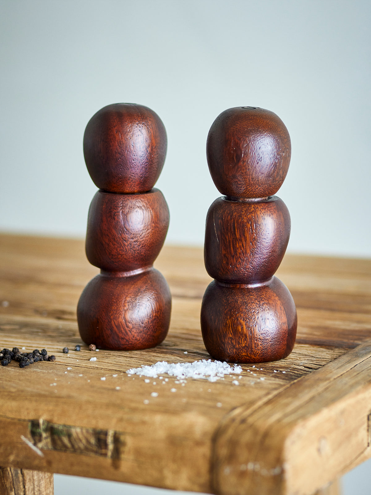 Salvi dark wooden salt and pepper mills on a rustic wooden table beside scattered peppercorns and sea salt