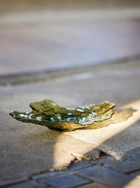 Aiku olive green glass bowl styled on a stone floor beside marble side tables
