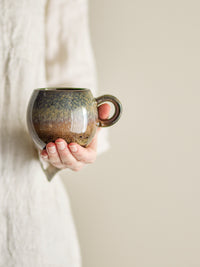 Paula cup in brown reactive glaze stoneware, rounded retro shape, held in hand, 275ml
