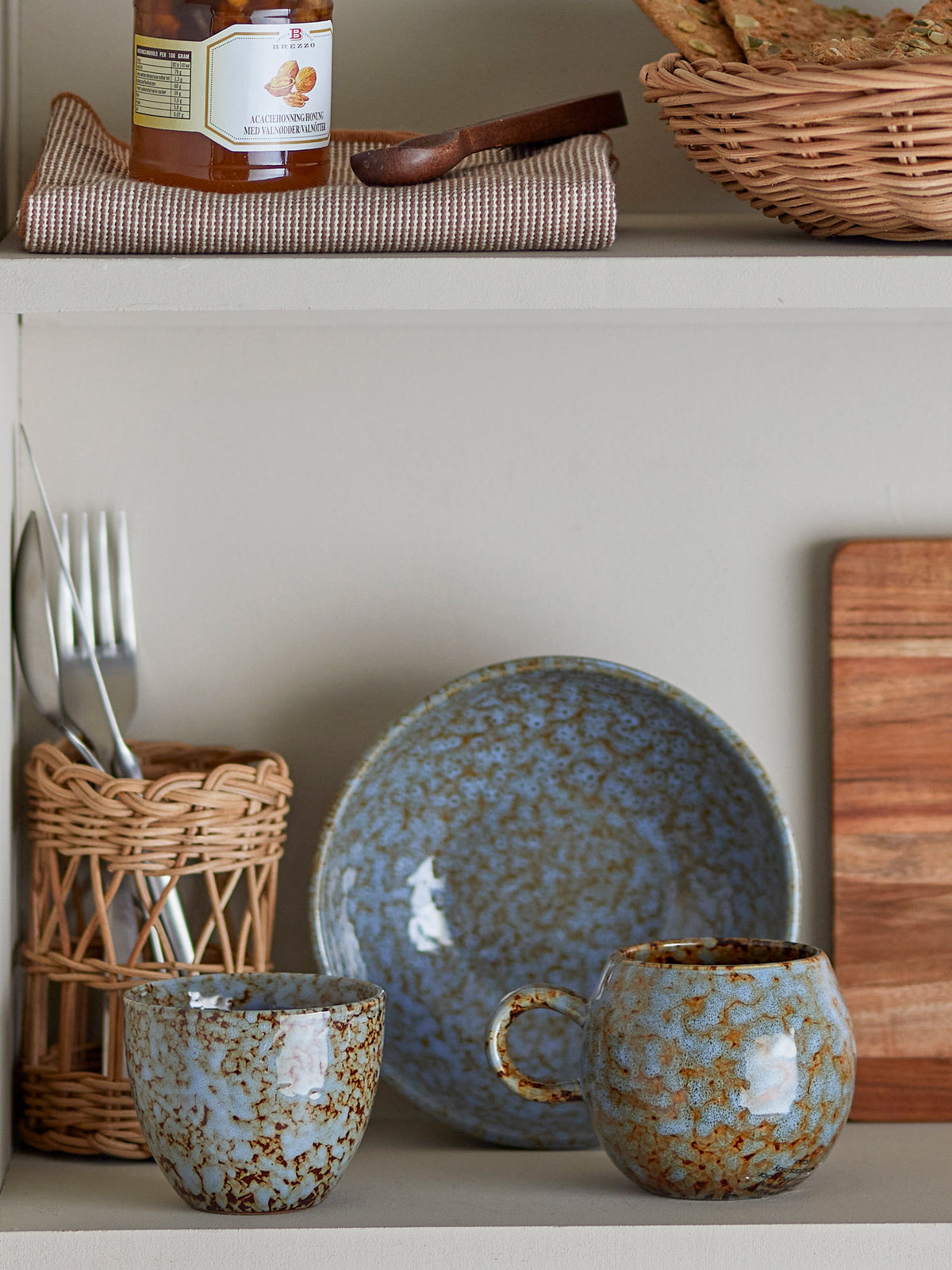 Ceramic tableware with speckled design on a shelf with wooden basket and jar.