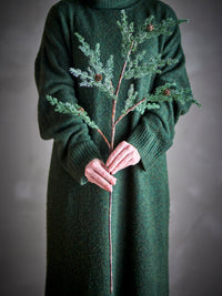 Person in a dark green knitted dress holding the frosted green Pine Stem with small cones