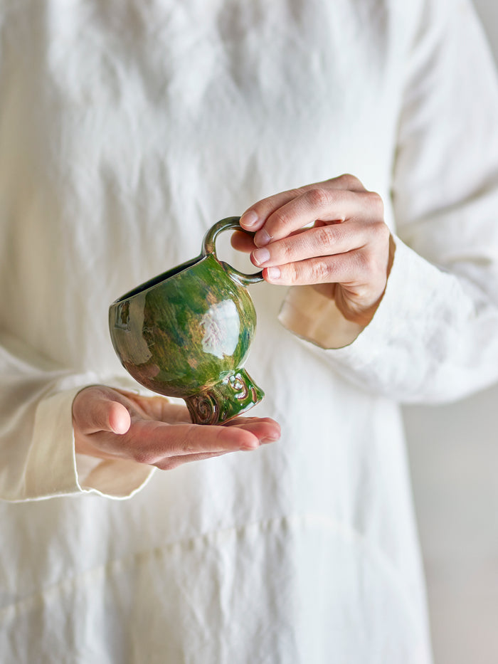 Avonlea cup green stoneware mug with artisan glaze, held in hand
