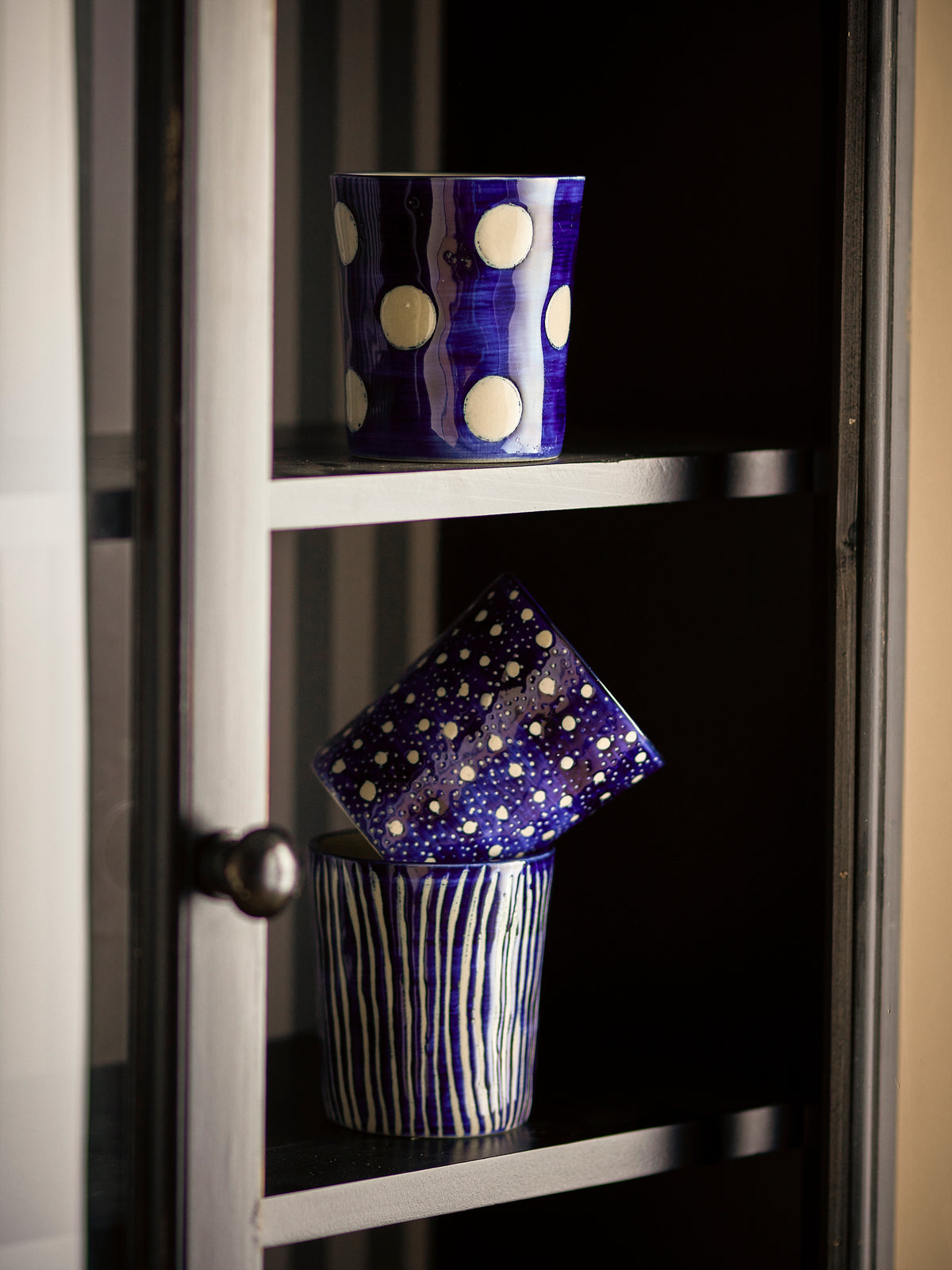 Minoa blue stoneware mugs with hand-applied patterns stacked in a kitchen cabinet

