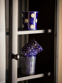 Minoa blue stoneware mugs with hand-applied patterns stacked in a kitchen cabinet
