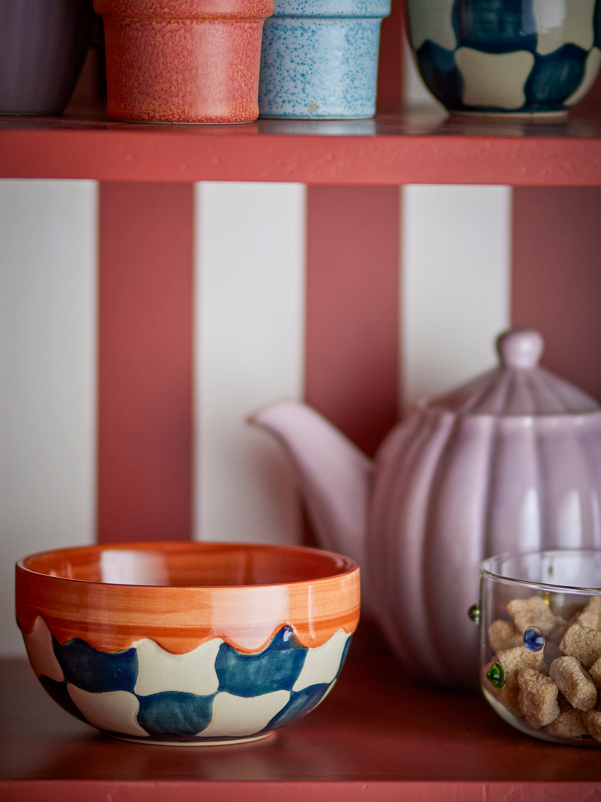 Check bowl in blue, beige, and terracotta hand-painted stoneware, styled on a kitchen shelf
