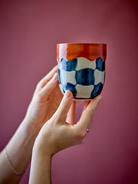 Check cup in blue and cream checkered stoneware with red rim, held in hand
